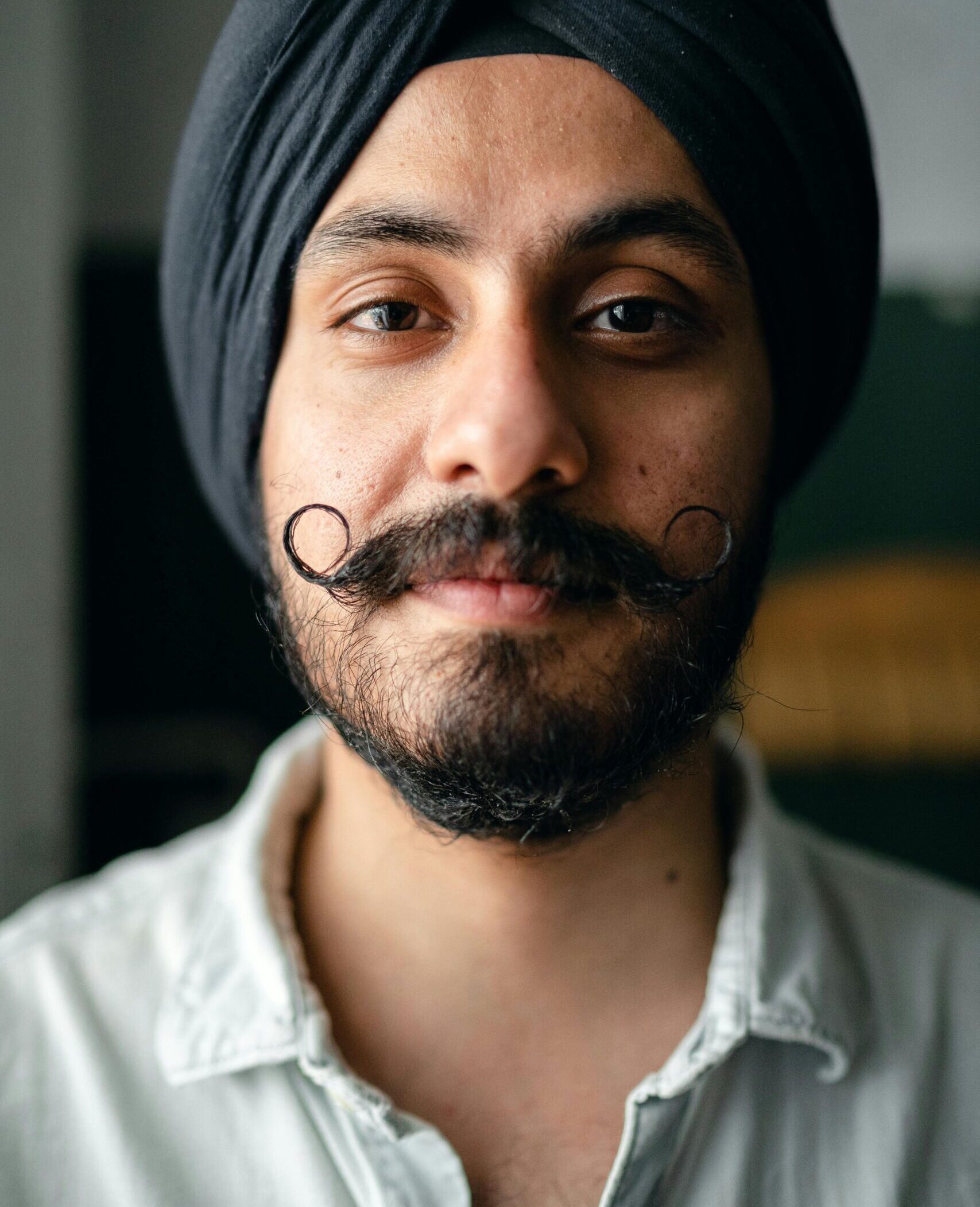 Young bearded Sikh man in traditional turban and shirt smiling and looking at camera