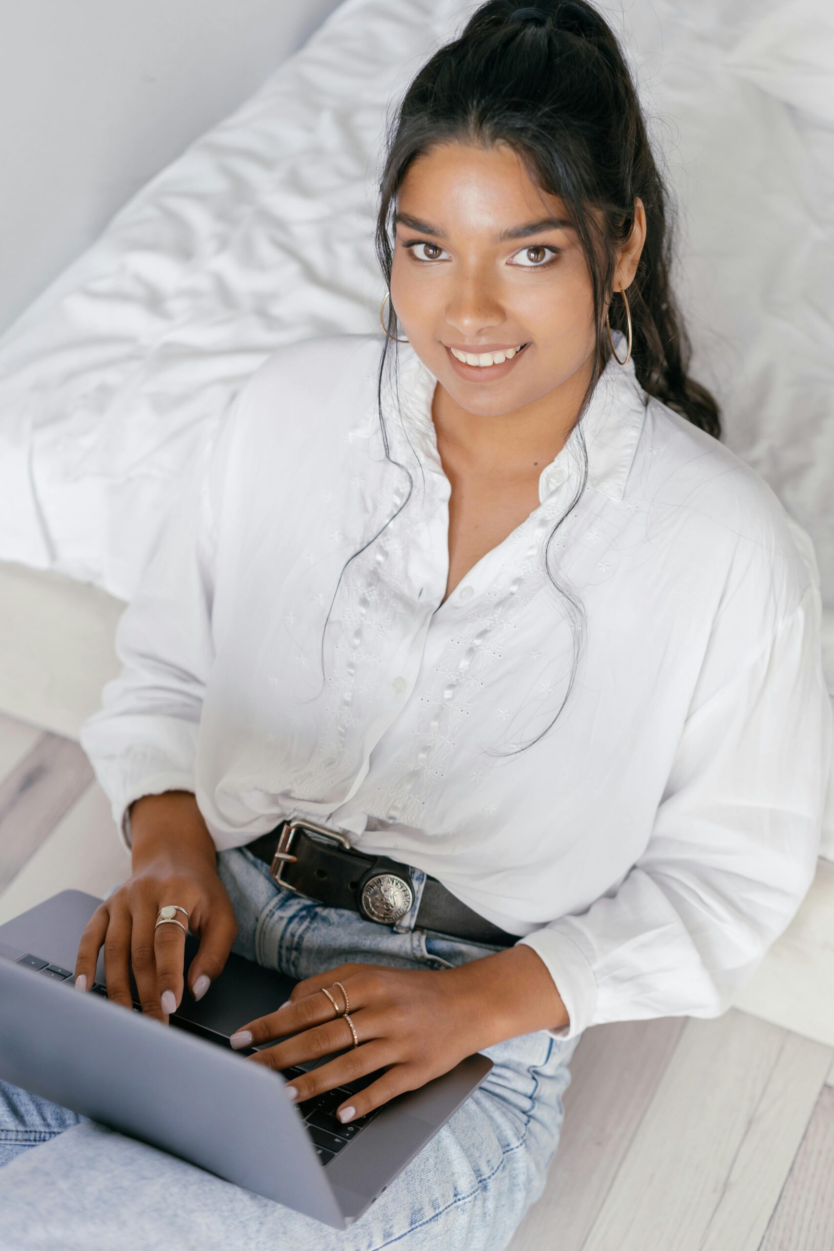 Smiling young woman typing on a laptop indoors, top view angle.